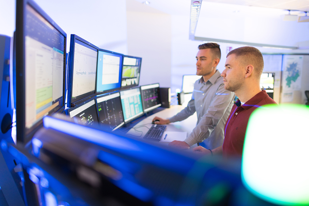 Bild mit zwei männlichen Personen stehend vor mehreren Bildschirmen im Störungsmanagement