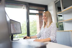 Digitale Straßenerfassung GeoScan Eine Frau steht an einem Schreibtisch, schaut auf die Bildschirme und betätigt die Computermaus