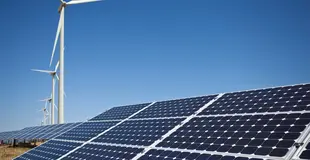 Photovoltaik-Anlage im Vordergrund mit mehreren Windkrafträdern im Hintergrund. Strahlend blauer Himmel. 