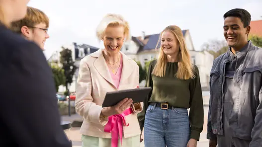Gruppe junger Menschen im Gespräch mit einer Frau, die ein Tablet in der Hand hält