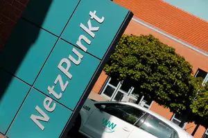 WWN Netzpunkt Der Schriftzug "NetzPunkt" auf einer pastellfarbenen Wand vor einem Gebäude. Hinter der Wand steht ein weißes Auto mit Westfalen Weser Logo