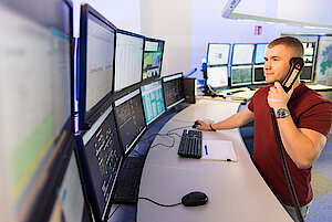 Eine Person stehend und telefonierend vor mehreren PC-Bildschirmen