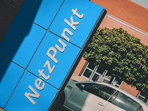 Ein blaues NetzPunkt‑Schild steht vor einem Gebäude mit geparktem Fahrzeug.