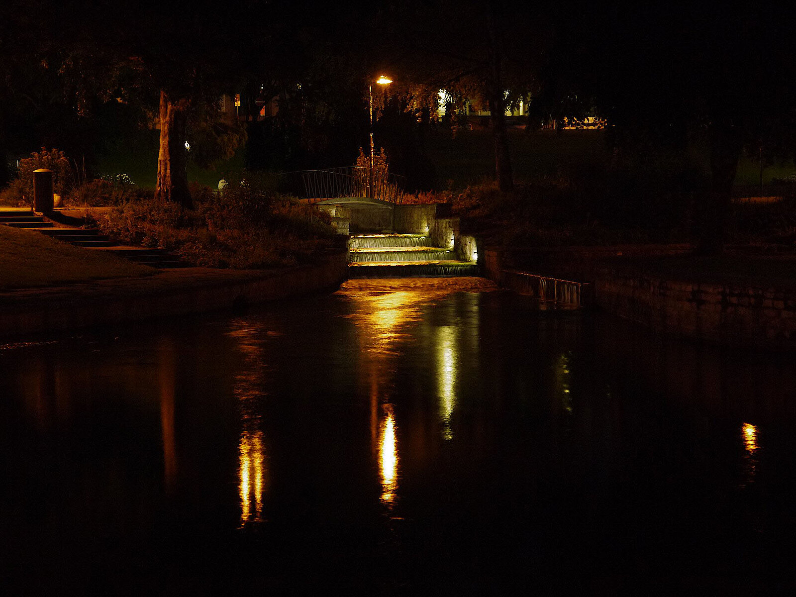 Beleuchtete Flussstufen und Brücke im Paderquellgebiet bei Nacht