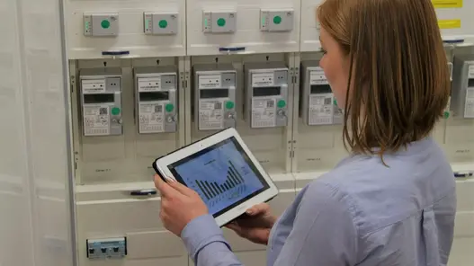 Eine Frau steht vor Zählern und hat ein Tablet in den Händen