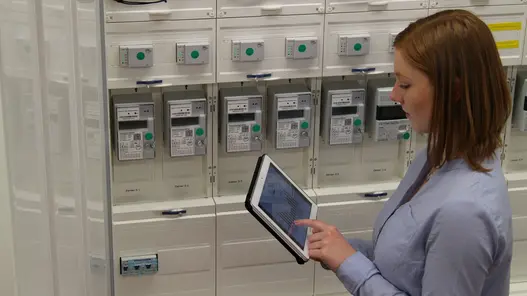 Eine Frau steht mit einem Tablet in der Hand vor Zählern und tippt etwas in das Tablet