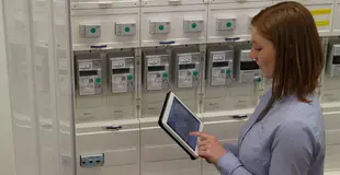 Eine Frau steht mit einem Tablet in der Hand vor Zählern und tippt etwas in das Tablet